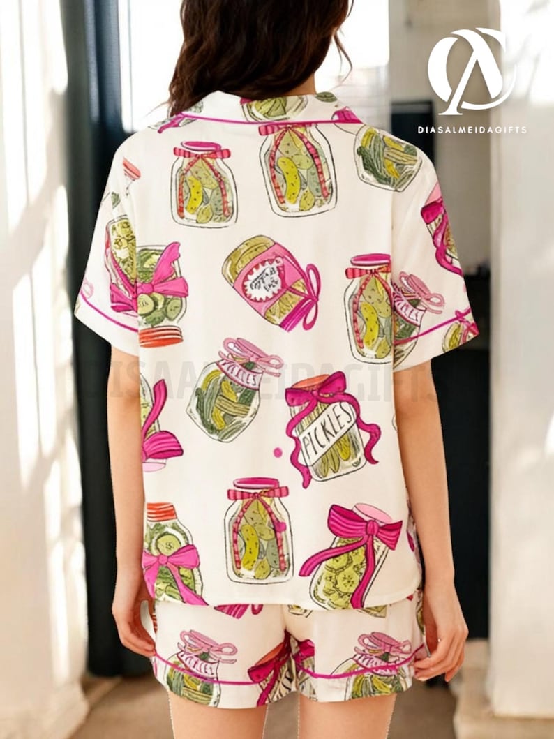 a person wearing a white shirt with a pattern of colorful illustrations of jars and pickles, along with pink bows.