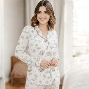 A smiling woman wearing a white pajama top with a pattern of cartoon characters is standing in a room.