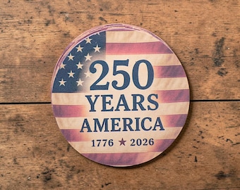Puede incluir: Una pila de posavasos redondos con un diseño de la bandera estadounidense. Los posavasos presentan el texto "250 YEARS AMERICA 1776 2026" en azul marino. El fondo tiene un aspecto vintage y desgastado.