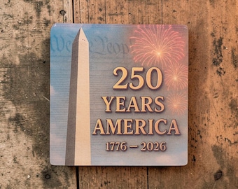 Puede incluir: Posavasos cuadrado con un diseño patriótico. Presenta el Monumento a Washington, fuegos artificiales y el texto "250 YEARS AMERICA 1776-2026". El fondo tiene un cielo azul y las palabras "We the People".