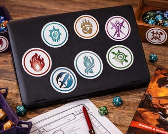 May include: A black laptop covered in circular stickers with fantasy-themed symbols. Dice, a Player's Handbook, and dice trays are arranged on a wooden surface, suggesting a tabletop role-playing game.