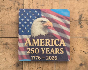 Puede incluir: Posavasos cuadrado con una bandera estadounidense y un águila calva. El posavasos tiene la palabra "AMERICA" en letras doradas, junto con "250 YEARS 1776-2026". El fondo muestra la bandera estadounidense con rayas rojas y blancas y estrellas azules.