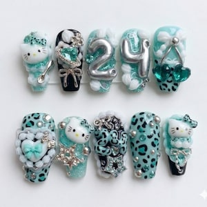 Peut inclure: Un ensemble de dix faux ongles avec divers motifs. Les ongles présentent un mélange de couleurs turquoise, noir et blanc. Certains ongles ont des motifs Hello Kitty, tandis que d'autres ont des imprimés léopard, des nœuds et des embellissements argentés.
