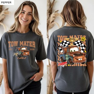 May include: Dark grey t-shirt with a cartoon image of Tow Mater from the film Cars. The front displays "Tow Mater" and "Cars". The back shows Mater with chequered flags and the text "Piston Cup" and Route 66.