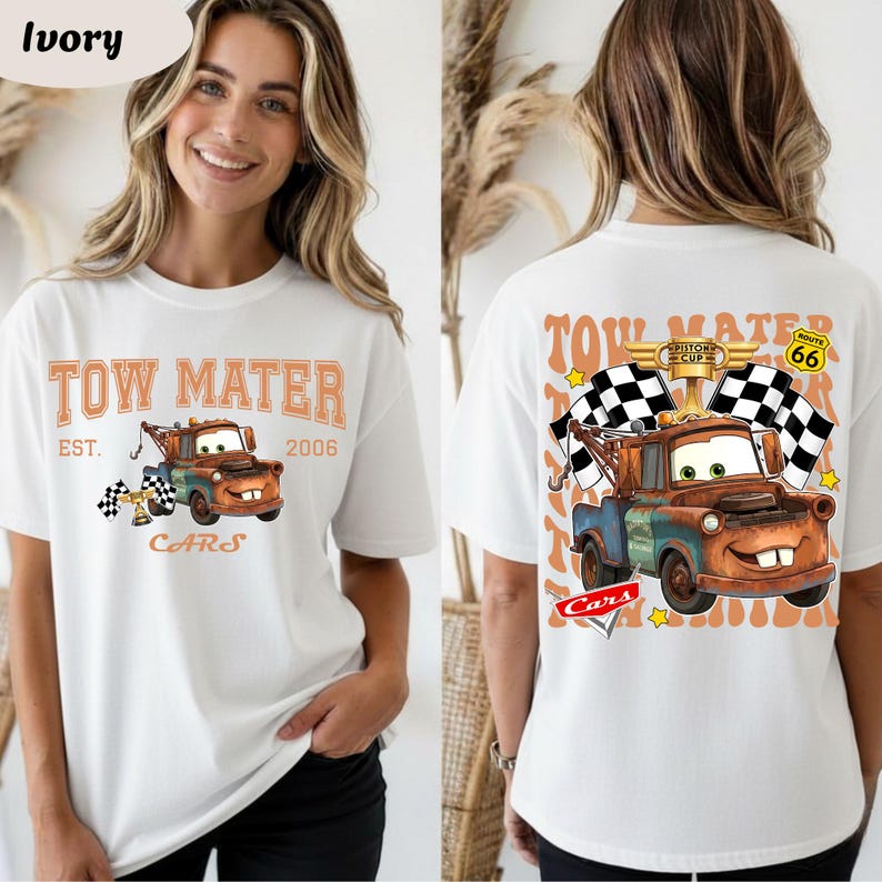 May include: Ivory-coloured t-shirt featuring a cartoon image of Tow Mater from the Cars film. The front design includes the text "TOW MATER EST. 2006 CARS" with a checkered flag. The back design shows Mater with checkered flags and the text "PISTON CUP ROUTE 66".