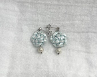 May include: A pair of light blue earrings with a woven knot design and silver-colored ball accents. The earrings are displayed on a white background.