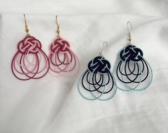 May include: Three pairs of handmade earrings. Two pairs are in shades of pink and red, and the third pair is navy blue and teal. Each earring features a knotted top and a teardrop-shaped design.