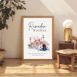 Puede incluir: Un cuadro enmarcado con las palabras "Ramadan Mubarak". La imagen presenta una ilustración en acuarela de una mezquita con cúpulas y minaretes rosas, rodeada de flores. El texto en la parte inferior dice: "Cuando llega el Ramadán, se abren las puertas del Paraíso."