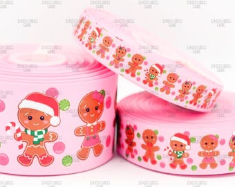 May include: Pink ribbon rolls with a repeating pattern of gingerbread people in Santa hats, scarves, and dresses. The ribbon is decorated with green and pink polka dots, perfect for holiday crafts and gift wrapping.