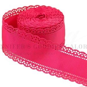 May include: A roll of hot pink grosgrain ribbon featuring a scalloped eyelet lace edge on both sides. The ribbon has a distinct ribbed texture running horizontally along the center, with a delicate, repeating circular cutout pattern along the borders.