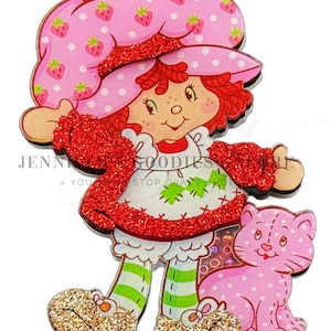 May include: A red and white cartoon character with red hair and a pink hat with white polka dots and strawberries. The character is holding a pink cat with white polka dots. The character is wearing a red sweater and green and white striped pants. The character is standing on a white background.