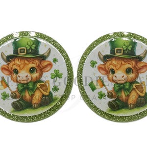 May include: Two round, glitter-edged images feature a cartoon Highland cow wearing a green leprechaun hat and bow tie. The cow holds an Irish flag and sits next to a harp. Shamrock accents surround the cow.