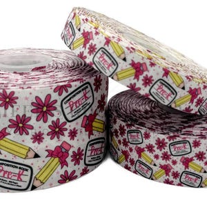 May include: Three rolls of white and pink ribbon with a repeating pattern of pink flowers, yellow pencils, and the text "Composition Book Pre-K".