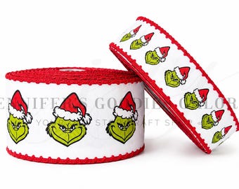 Può includere: Un rotolo di nastro bianco con un motivo ripetuto di volti verdi del Grinch che indossano cappelli da Babbo Natale rossi e bianchi. Il nastro ha un bordo rosso testurizzato cucito su entrambi i lati. Il testo JENNIFERS GOODIES GALORE è visibile.