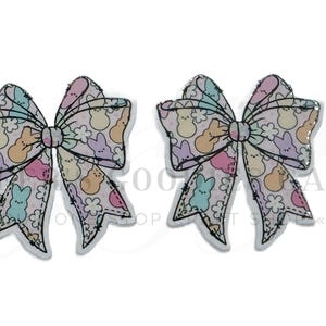 May include: Two decorative bow-shaped accessories. Each bow features a pastel pattern of Easter Peeps and flowers on a white background. The bows have a black outline and are suitable for crafting or embellishing projects.
