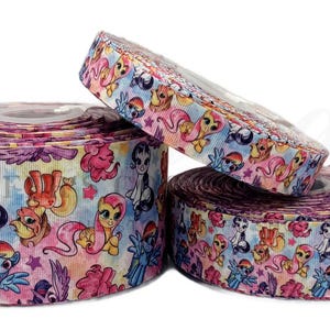 May include: Three rolls of decorative ribbon featuring a colorful cartoon pony design. The ribbon has a watercolor effect with pink, blue, yellow, and purple hues. The pony characters are in various poses, with stars and floral accents.