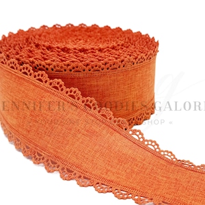 May include: A roll of burnt orange fabric ribbon featuring a textured linen-like weave and a delicate scalloped lace trim along both edges. The ribbon is coiled into a spool shape, displaying the consistent solid color and intricate lace detail.