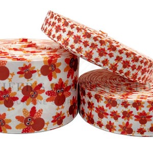 May include: Three rolls of decorative ribbon with a Thanksgiving theme. The ribbon features a repeating pattern of cartoon turkeys in shades of orange, red, and brown on a white background. One roll is partially unrolled.