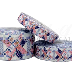 May include: Three rolls of decorative ribbon with a patchwork quilt design. The ribbon features a pattern of pink, blue, and white floral and geometric shapes. The rolls are of varying sizes, with the largest roll in the foreground.