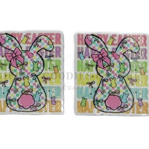 May include: Two square Easter-themed decorations with a bunny design. The bunnies have a pink bow and a pink belly. The background has the words "Happy Easter" and a colorful checkered pattern. The decorations are white with a glossy finish.