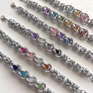 May include: Five silver chainmail bracelets with colorful beads. Each bracelet features a different color of beads, including purple, pink, green, orange, and blue. The bracelets have a lobster claw clasp.