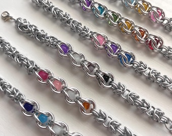May include: Five silver chainmail bracelets with colorful beads. Each bracelet features a different color of beads, including purple, pink, green, orange, and blue. The bracelets have a lobster claw clasp.