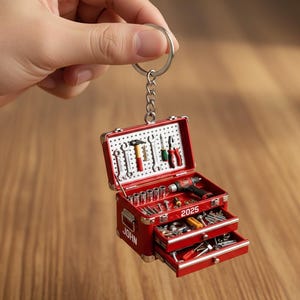 May include: Miniature red toolbox keychain with silver hardware, open to reveal tiny tools. The toolbox has two drawers and a pegboard. The name "JOHN" and the year "2025" are visible on the toolbox.