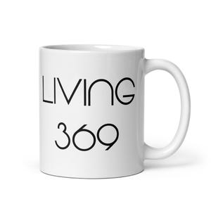 May include: White ceramic mug with the words "LIVING 369" printed in black. The mug has a curved handle and a glossy finish. The text is in a sans-serif font.