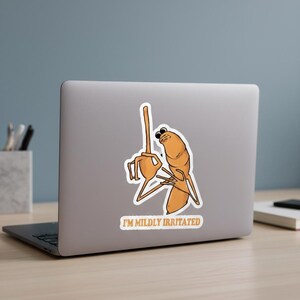 May include: A sticker featuring a cartoon character in shades of orange and brown, with the text "I'M MILDLY IRRITATED". The character is depicted with a frustrated expression and raised arms, suggesting annoyance.