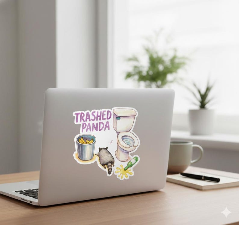 May include: A sticker featuring a cartoon raccoon, a toilet, a bucket of bananas, and a spilled bottle. The text "Trashed Panda" is above the illustrations. The sticker is on a laptop.