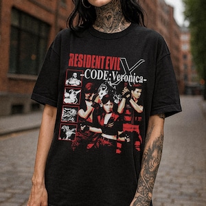 May include: Black t-shirt featuring the text "RESIDENT EVIL - CODE: Veronica-" in red and white. The shirt has a graphic of characters from the video game. The shirt is made of a soft material.