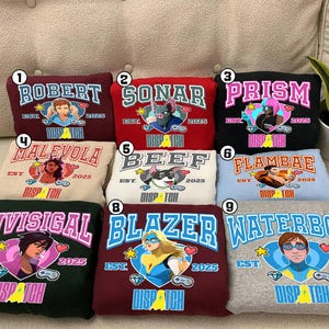May include: A collection of nine sweatshirts in various colors, each featuring a unique graphic design and text. The designs include names like "Robert," "Sonar," and "Prism," along with illustrations and the text "Dispatch" and "Est. 2025."