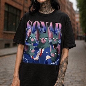May include: Black t-shirt featuring a cartoon graphic of bat-like creatures in suits with the word "SONAR" in a gradient font. The bats have green skin, pink ears, and pig-like snouts. Lightning bolts are in the background.