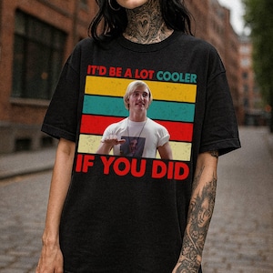 May include: Black t-shirt with a retro design featuring the phrase "IT'D BE A LOT COOLER IF YOU DID" in red and white text. The design includes a picture of a man and colorful horizontal stripes.