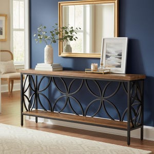 May include: A long, rectangular console table with a dark wood top and a black metal base. The base features a decorative, repeating floral pattern. The table is adorned with a mirror, artwork, and decorative items.