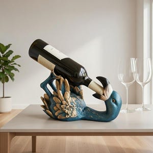 May include: A blue and gold decorative wine bottle holder in the shape of a bird, holding a wine bottle. The bird has a long neck and beak, with a detailed feather design. The wine bottle is black with a white label.