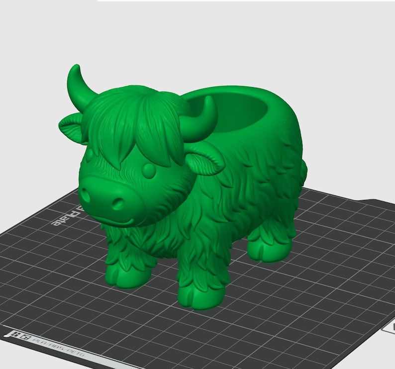 May include: A green Highland cow planter with a detailed, textured design. The planter has a round opening on its back for plants. The cow has horns, a fluffy mane, and a friendly face. The planter is a decorative item.