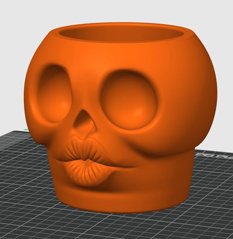 May include: Orange skull-shaped planter with large eye sockets and a puckered mouth. The planter is a solid color and has a smooth surface. The skull planter is a decorative item.