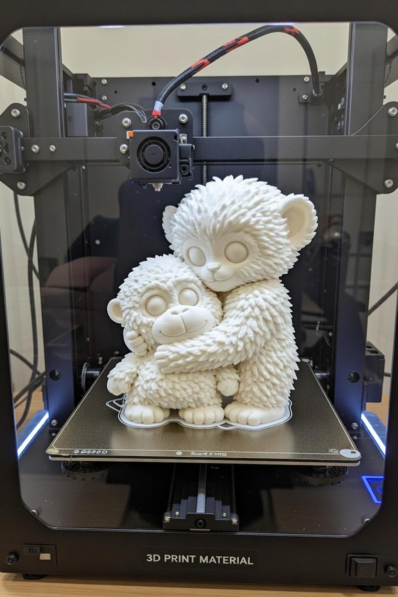 May include: A 3D-printed sculpture of two white monkey-like figures embracing. The larger figure hugs the smaller one. The figures are on a 3D printer platform. The printer has a black frame and the text "3D PRINT MATERIAL".