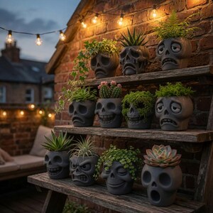 May include: A collection of gray skull-shaped planters filled with various succulents and greenery. The planters are arranged on wooden shelves against a brick wall, illuminated by string lights. The skull designs have different facial expressions.