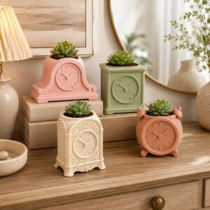 May include: Four decorative planters shaped like vintage clocks, each containing a small green succulent. The planters are pastel pink, sage green, cream, and terracotta, featuring moulded clock faces with hands and numbers on the front surfaces.