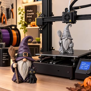 May include: A 3D printer with a gray gnome figurine on the print bed, featuring a tall hat, a broom, and a small cat. In the foreground, a finished purple gnome figurine with a black belt, a broom, and a black cat stands on a wooden surface.