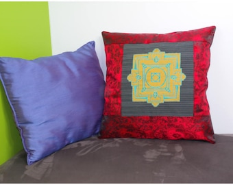May include: Two decorative throw pillows, one is a deep red with a gold and turquoise mandala design, the other is a light purple.