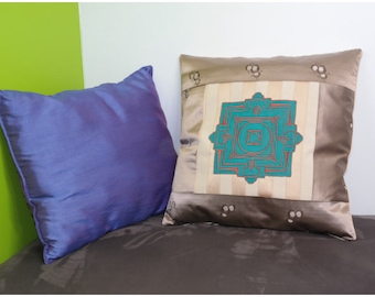 May include: Two decorative throw pillows, one blue and one brown with a teal and red geometric design. The pillows are on a brown couch.