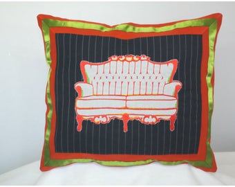 May include: A decorative pillow with a black and white striped background and a red and white silhouette of a couch. The pillow has a green and orange border.