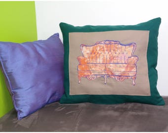 May include: A green and beige throw pillow with a drawing of a vintage couch in blue and orange.