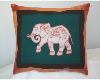 May include: A decorative pillow with an orange border and a green center featuring a white embroidered elephant with red details.