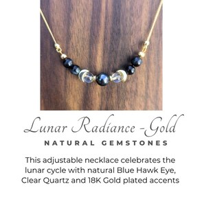 Puede incluir: Un collar de cadena dorada con una disposición central de cuentas esféricas azul oscuro, dos cuentas de cuarzo transparente y dos dijes de media luna dorados. El texto dice: Lunar Radiance - Gold NATURAL GEMSTONES This adjustable necklace celebrates the lunar cycle with natural Blue Hawk Eye, Clear Quartz and 18K Gold plated accents.