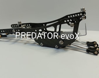 May include: Black and silver mechanical device with the text "PREDATOR evoX". The device has multiple holes and connecting rods. The device is on a white surface.