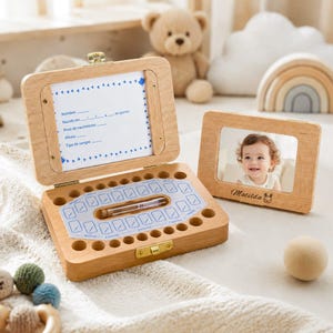 May include: A light-coloured wooden keepsake box with a hinged lid featuring a printed birth record card and a series of circular holes for storing teeth. Beside it sits a matching wooden picture frame displaying a photo of a smiling child.